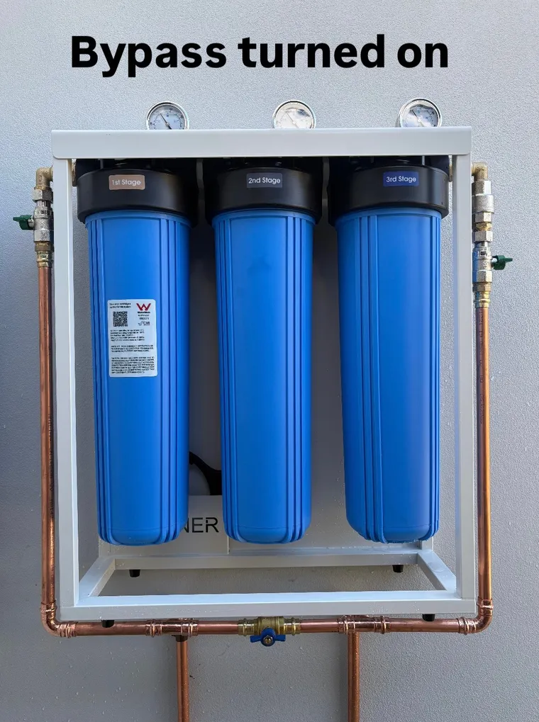 Whole house filtration system with the bypass turned on: inlet and outlet valve handles at a right angle to the pipes and the bypass valve underneath turned on