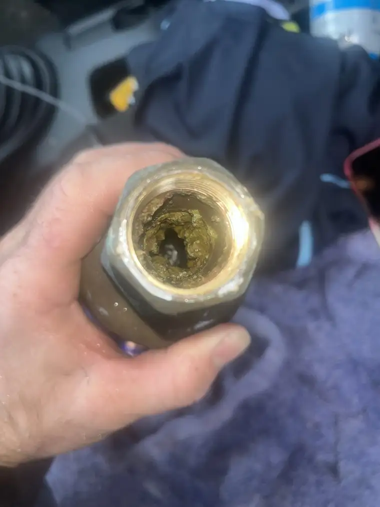 The inside of a local client's brass inlet pipe heavily clogged with green and brown mineral build-up and corrosion