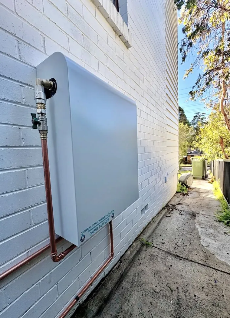 Slimline whole house water filtration system installed on a brick wall with copper plumbing