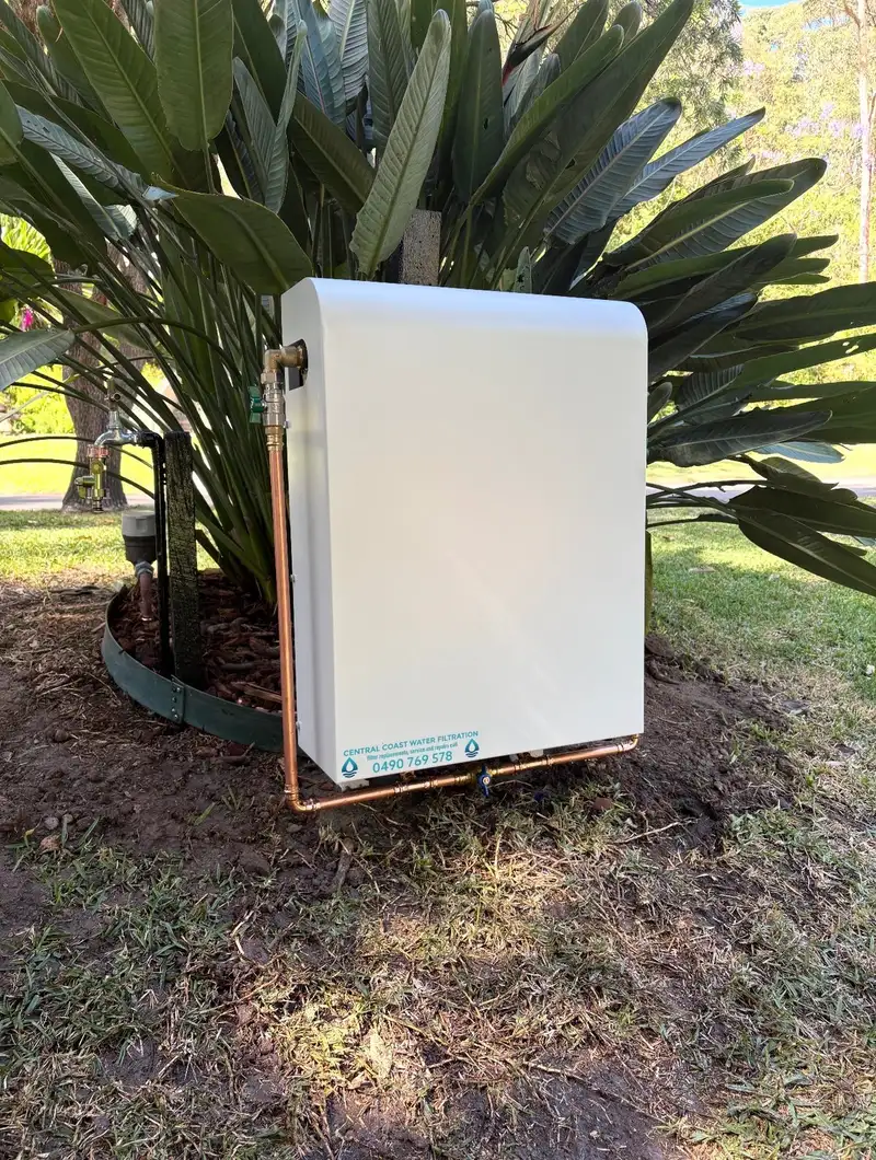 White powder-coated whole house water filtration system installed freestanding in a garden bed, plumbed in with copper pipe