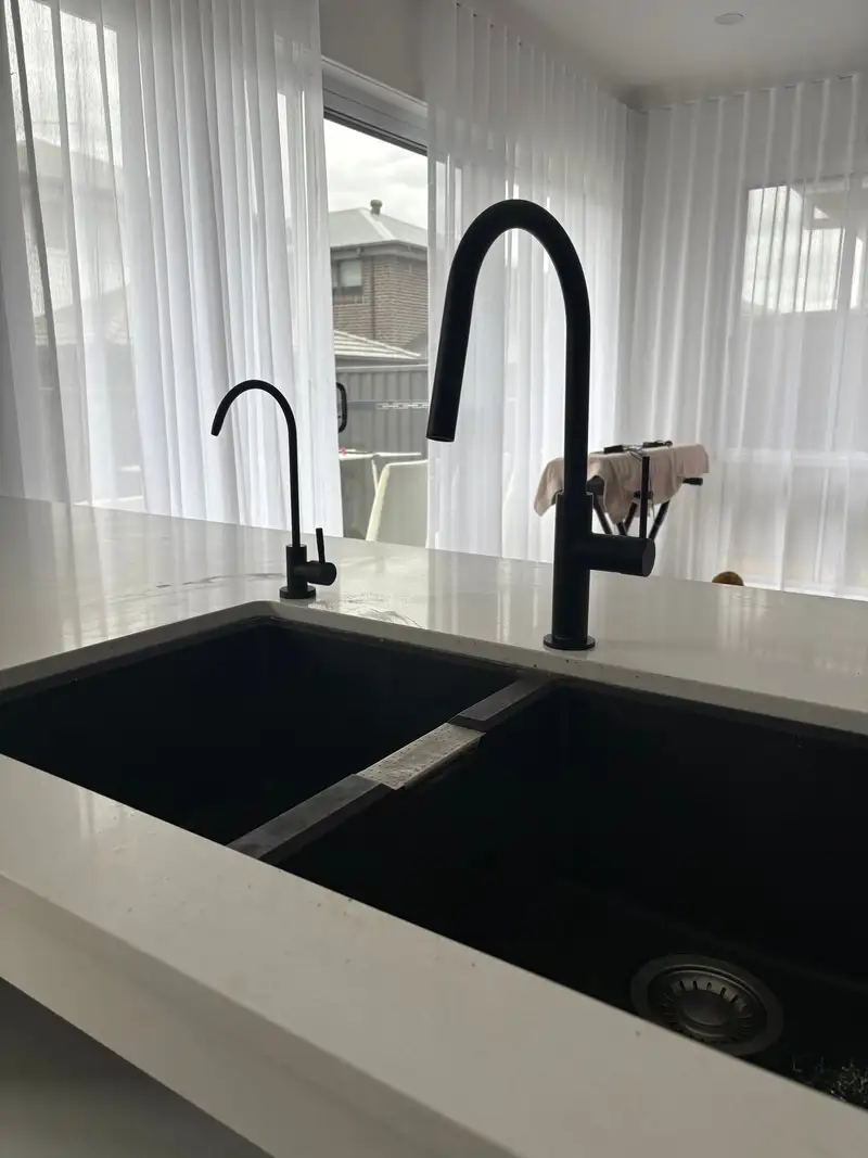Matte black filtered water tap beside a matching black mixer on a white stone island with a black sink
