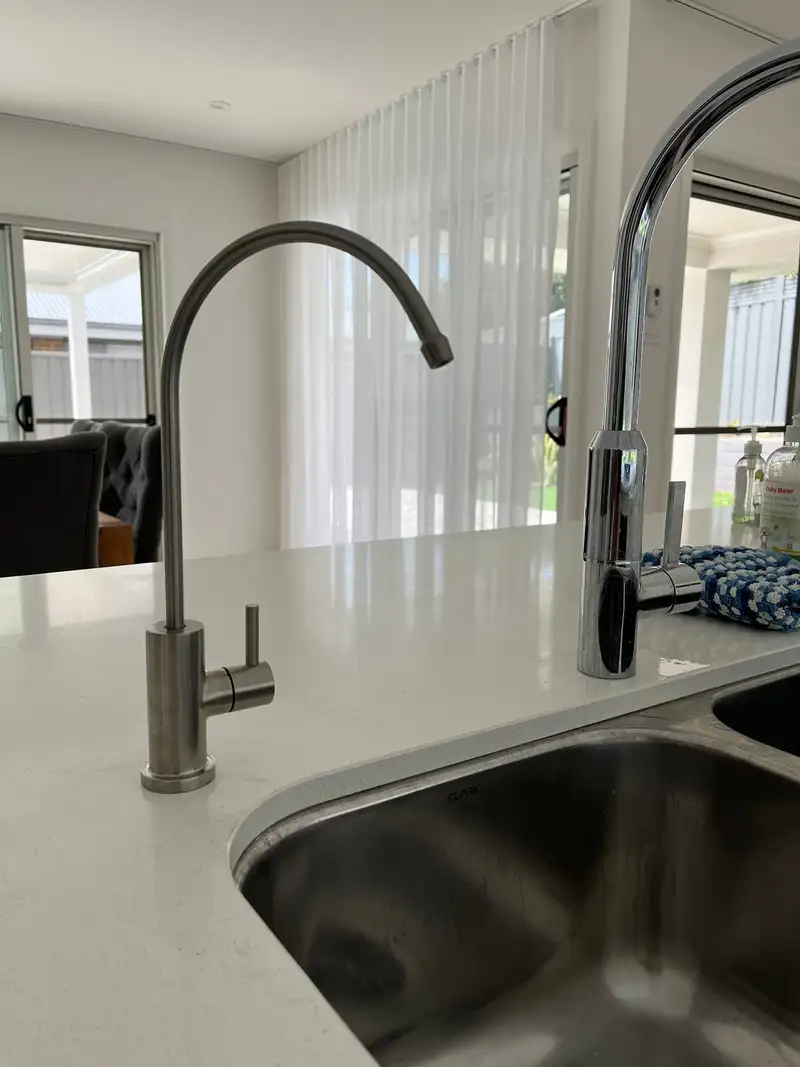 Brushed stainless filtered water tap on a white stone benchtop beside a chrome kitchen mixer