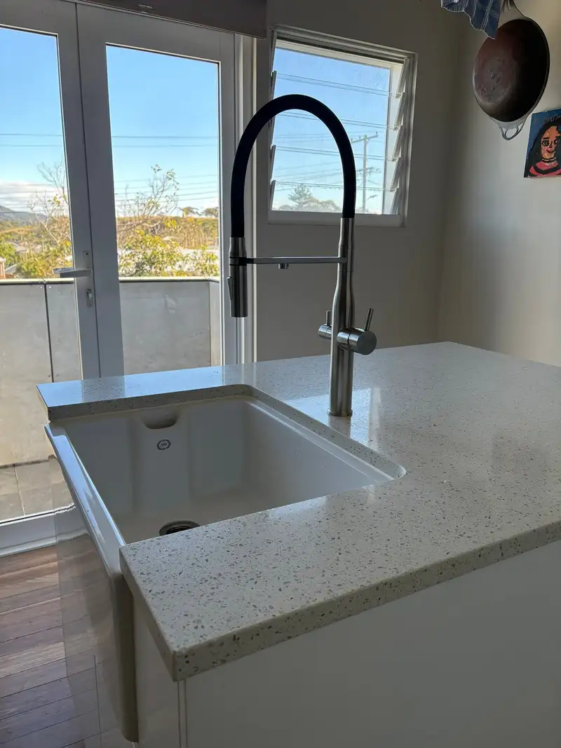 Stainless steel three-way pull-out kitchen tap with a black flexible spray hose and separate handles for filtered and mixed water, beside a white farmhouse sink